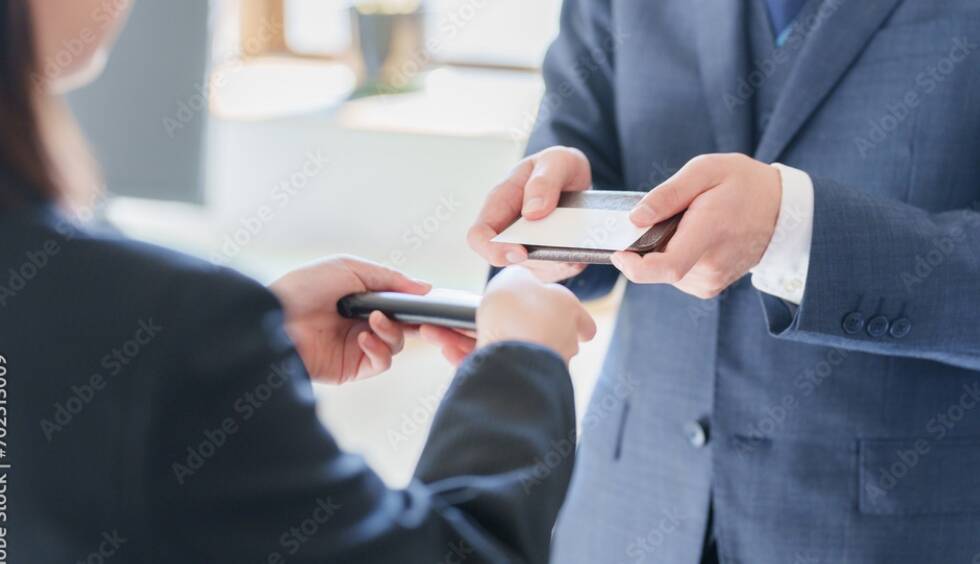 男性のビジネスマンが女性にスマートフォンを手渡しているシーンを描写した画像です。