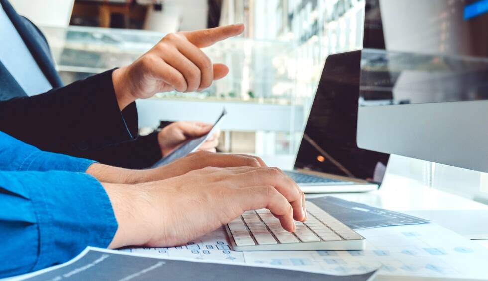 ビジネスパーソンがコンピュータで作業し、手を指し示している様子の画像です。